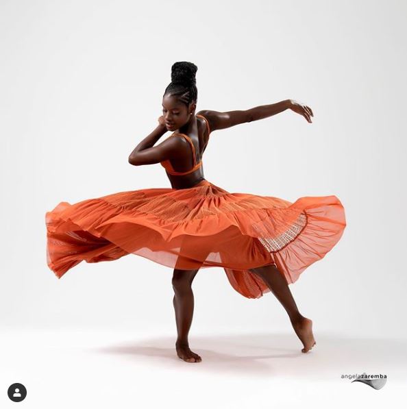 Ingrid Silva, jovem mulher negra, posa como bailaria com uma saia rodada laranja.