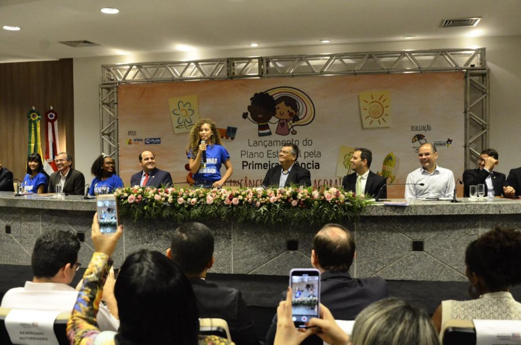 Menina adolescente discursa em um palco ao lado do governador do Estado do Maranhão. A imagem também mostra a plateia com celulares filmando a menina. A ação fez parte do movimento Meninas Ocupam de 2019.