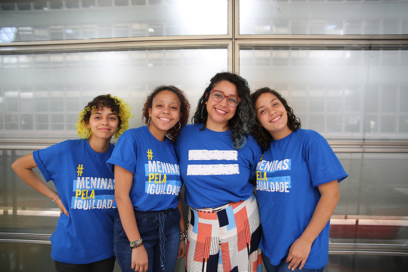 Três adolescentes meninas posam para foto junto a educadora do projeto Escola de Liderança para Meninas. As meninas vestem uma camiseta azul com a frase "Meninas pela Igualdade", da campanha da Plan International Brasil.