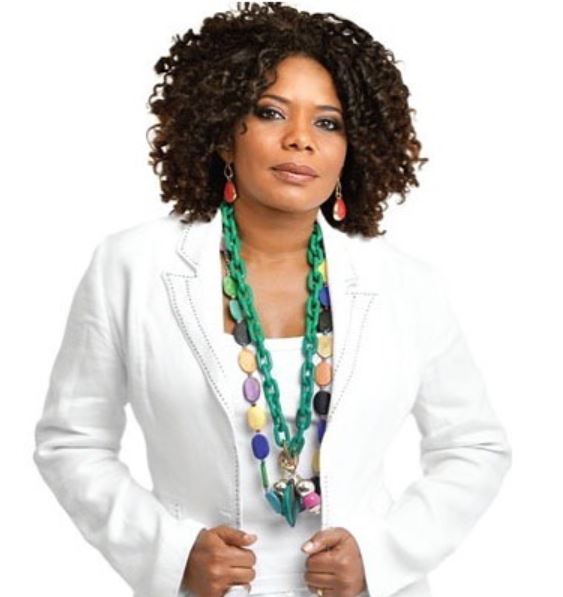 Margareth Menezes, cantora baiana de axé e nova embaixadora da Plan Brasil, posa de frente para uma foto. Ela veste um blazer branco e um colar colorido. Sua feição é mais séria.