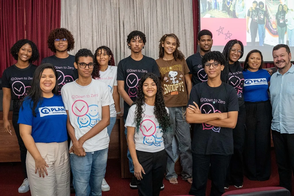 Grupo diverso de jovens e educadores do projeto Down To Zero posam juntos após atividade de conscientização sobre ambientes seguros para infância e juventude.