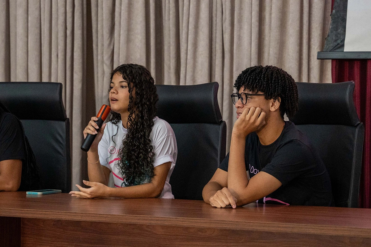 Jovens participantes do projeto Down To Zero debatem com microfone em mãos durante uma roda de conversa sobre proteção contra violência e exploração infantil.