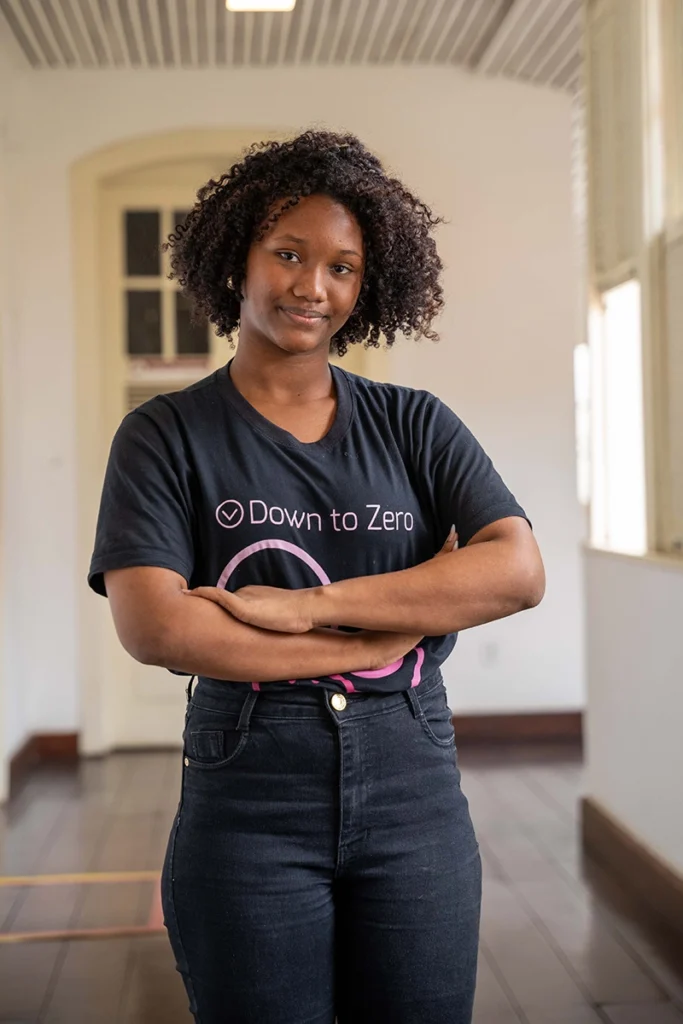 Jovem com camiseta do projeto Down To Zero posa com os braços cruzados, simbolizando o protagonismo de adolescentes na luta contra violências e abusos.
