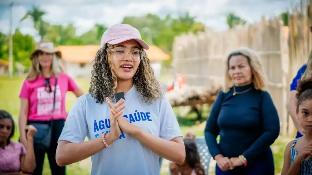 Jovem participante de projeto da Plan International Brasil falando em evento comunitário, representando ações de impacto social promovidas por empresas.