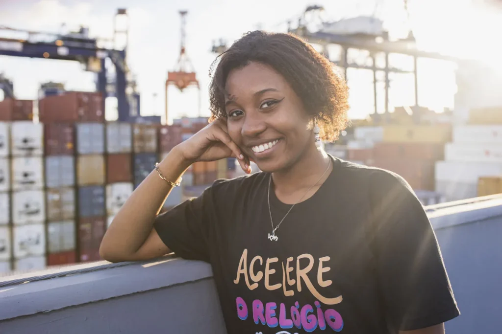 Jovem sorridente posa em frente a contêineres de porto, simbolizando o futuro profissional e a autonomia incentivados pela Escola de Liderança para Meninas.