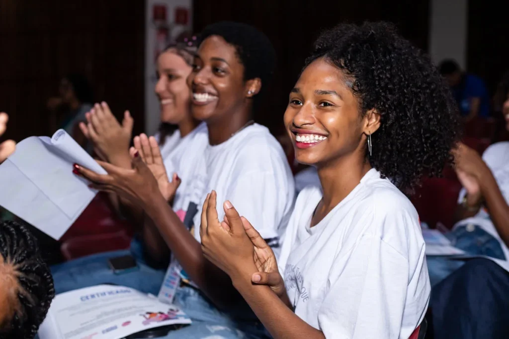 Jovens aplaudem e sorriem durante evento de entrega de certificados no projeto Escola de Liderança para Meninas, celebrando novas conquistas.