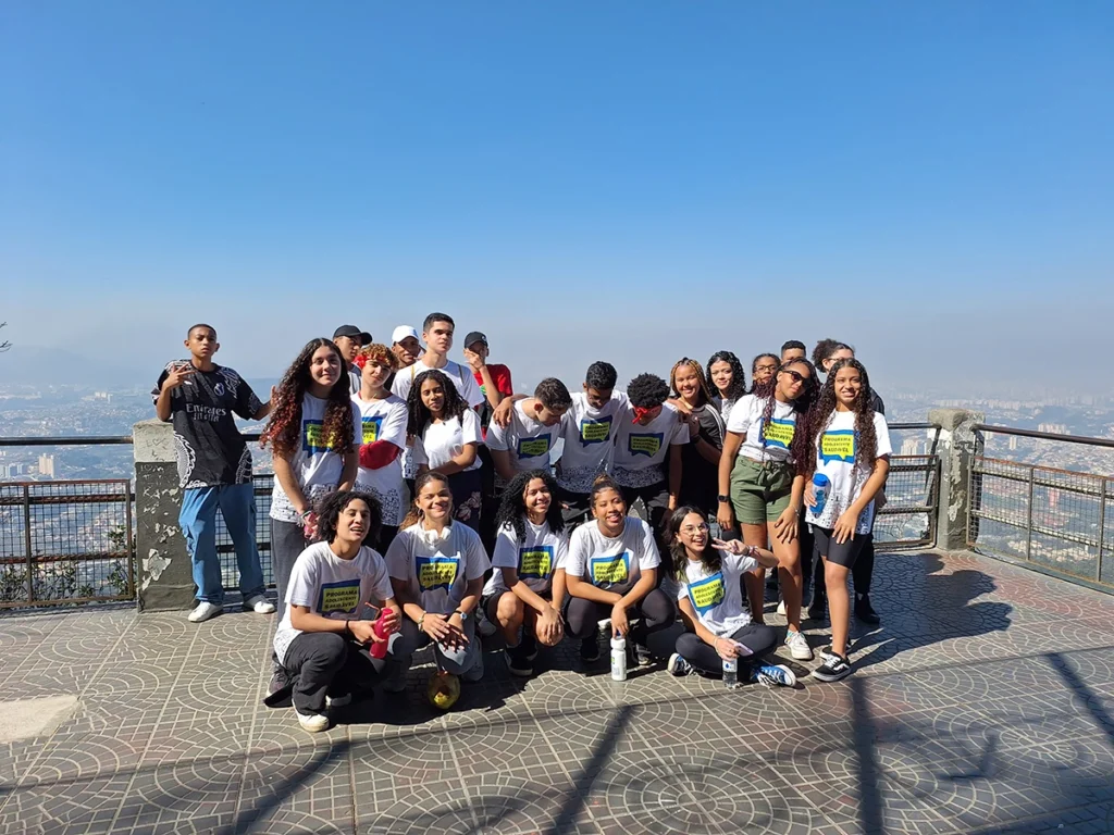 Grupo de adolescentes com camisetas do Programa Adolescente Saudável reunidos em mirante ao ar livre, promovendo saúde, integração e bem-estar.