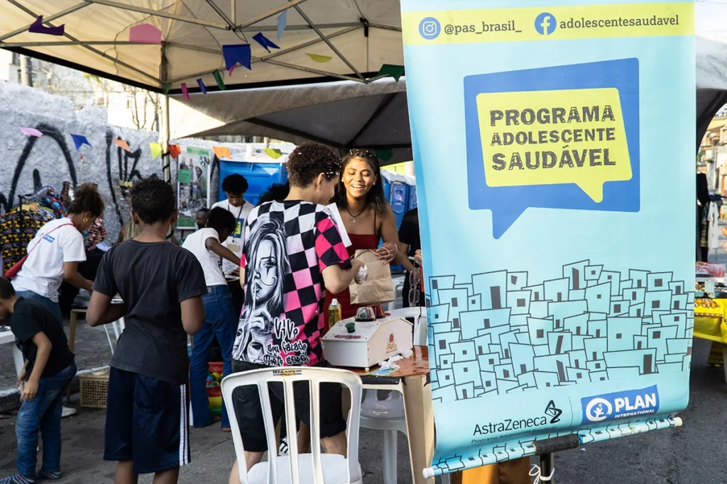 Jovens e crianças interagem em feira comunitária com estande do Programa Adolescente Saudável, promovendo saúde e protagonismo na adolescência.