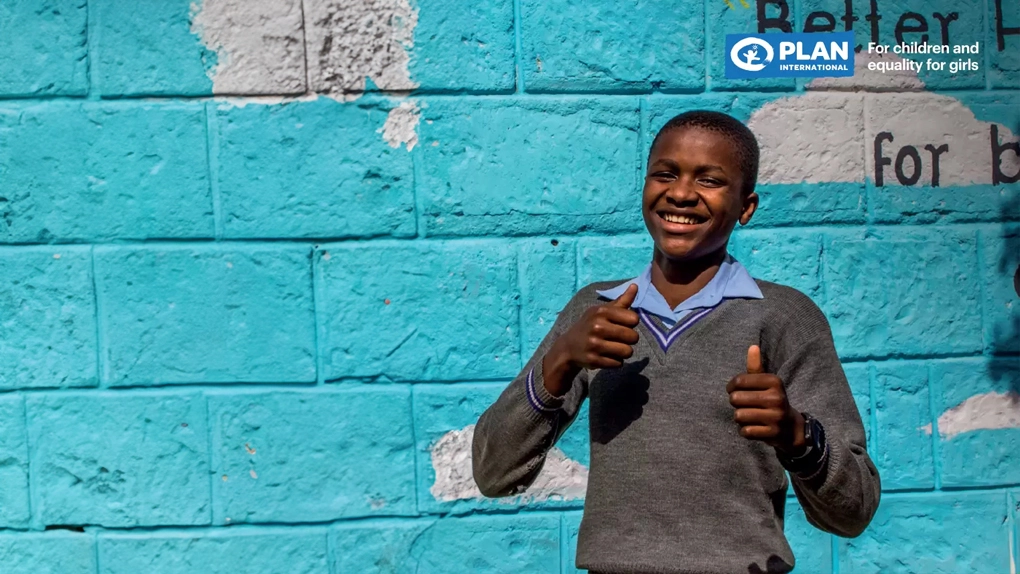 Dois adolescentes sorrindo e fazendo sinal de positivo em frente a um muro azul, representando bem-estar e saúde mental na adolescência