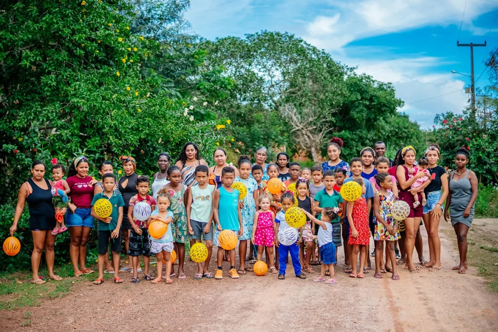 Grupo de crianças e adultos em uma comunidade quilombola segurando balões coloridos durante atividade do projeto Ciranda
