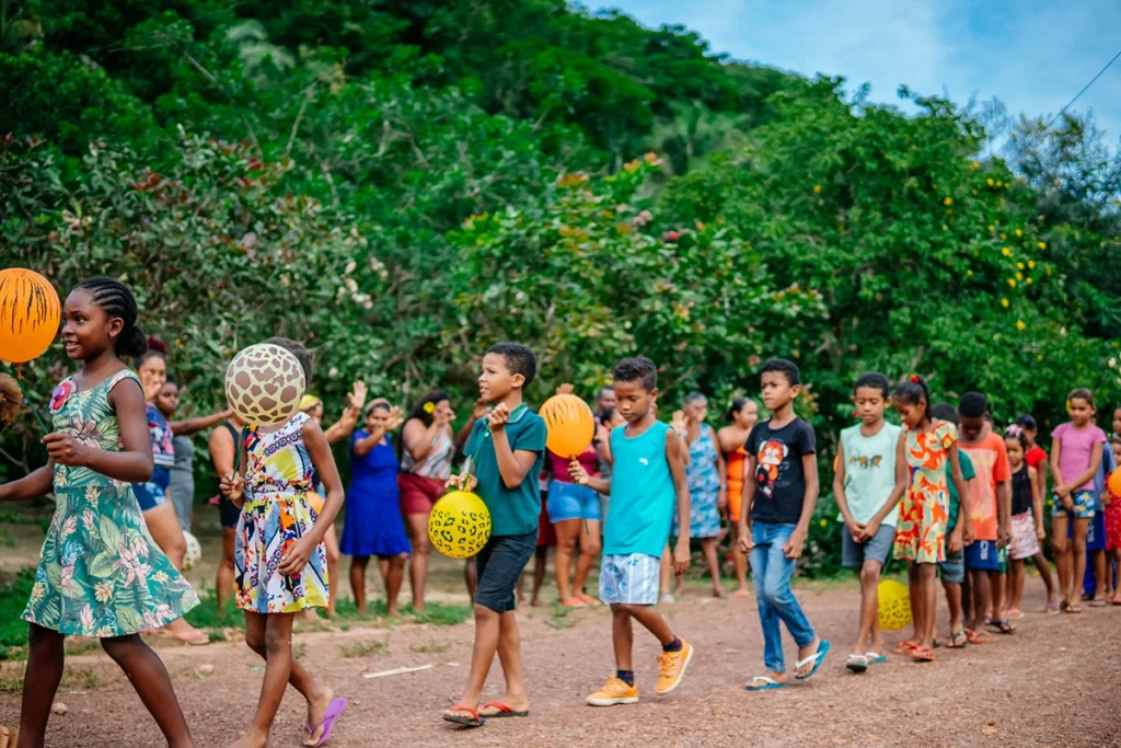 Crianças quilombolas caminhando em fila com balões coloridos durante atividade cultural do Projeto Ciranda